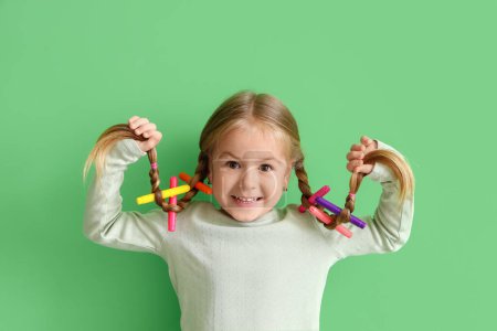 Téléchargez les photos : Petite fille mignonne avec des nattes et feutres stylos sur fond vert - en image libre de droit