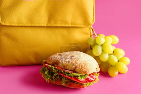 Téléchargez les photos : Sac à lunch avec sandwich et raisins sur fond rose - en image libre de droit