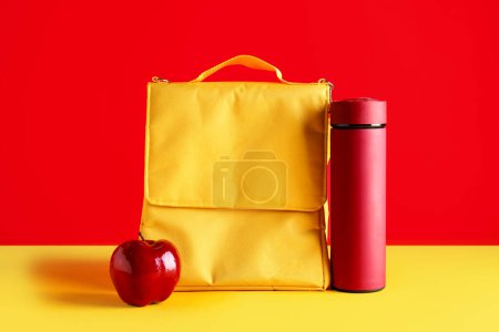 Téléchargez les photos : Sac boîte à lunch avec thermos et pomme fraîche sur fond de couleur - en image libre de droit