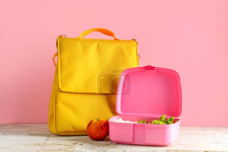 Téléchargez les photos : Sac et lunchbox avec nourriture savoureuse sur table blanche en bois près du mur rose - en image libre de droit