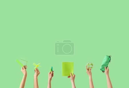 Téléchargez les photos : Mains tenant des fournitures scolaires sur fond vert - en image libre de droit