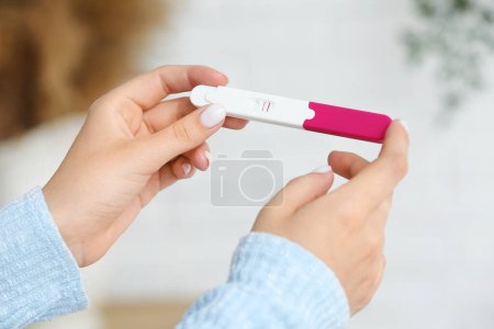 Weibliche Hände mit positivem Schwangerschaftstest auf verschwommenem Hintergrund, Nahaufnahme