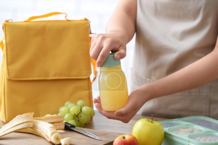Téléchargez les photos : Femme emballage bouteille de jus dans le sac de boîte à lunch dans la cuisine - en image libre de droit