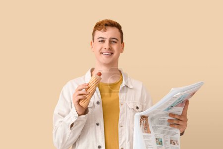Photo for Young man with tasty hot dog and newspaper on beige background - Royalty Free Image