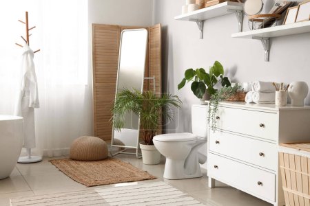 Foto de Interior del baño de luz con inodoro de cerámica, espejo y cómoda - Imagen libre de derechos