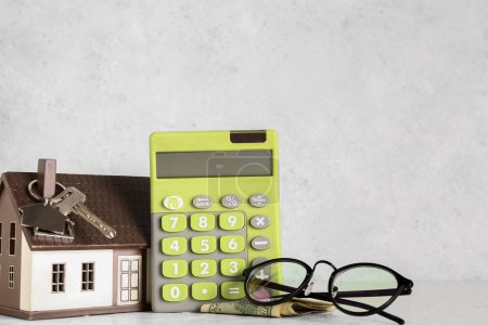 Calculator, keys, house model and eyeglasses on white table