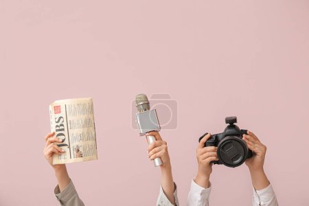 Female hands with newspaper, microphone and photo camera on color background