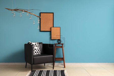 Foto de Elegante sillón negro y marcos de madera en blanco cerca de la pared azul - Imagen libre de derechos