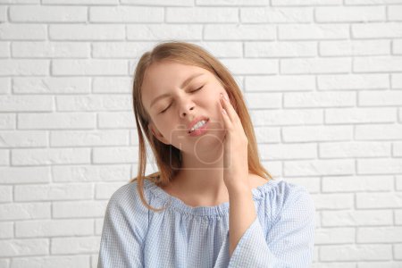 Téléchargez les photos : Jeune femme souffrant de mal de dents sur fond de brique blanche - en image libre de droit