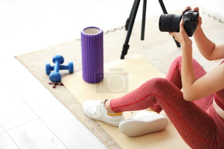 Photo for Beautiful young sport blogger recording video while training with roller and dumbbells at home - Royalty Free Image