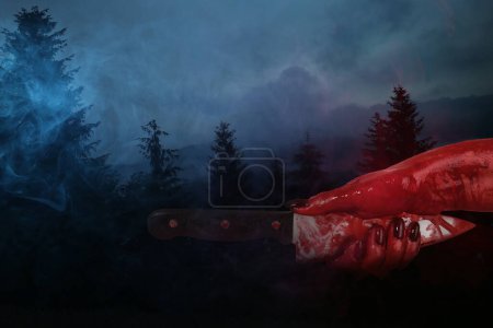 Hand with bloodstained knife in dark forest