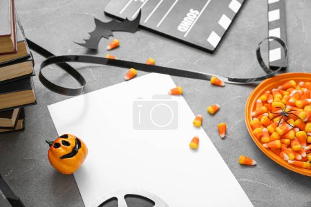 Téléchargez les photos : Clapperboard avec bobine de film, bonbons et papier blanc sur fond gris grunge. Fête d'Halloween - en image libre de droit