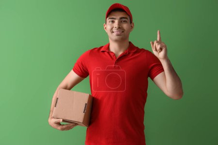 Photo for Male courier with parcel pointing at something on green background - Royalty Free Image