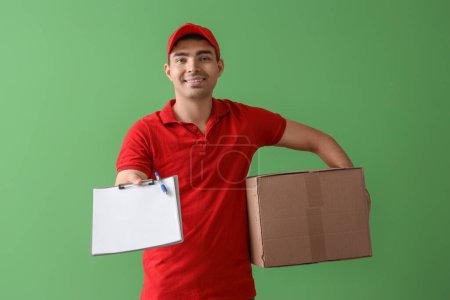 Foto de Mensajero masculino con portapapeles y paquete sobre fondo verde - Imagen libre de derechos
