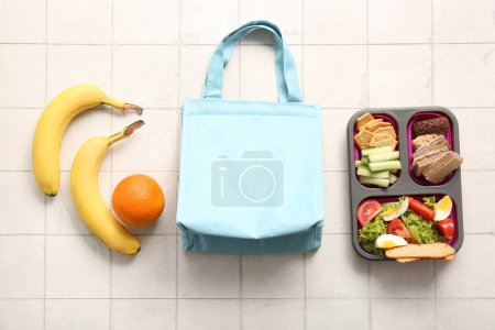 Téléchargez les photos : Sac, boîte à lunch avec de délicieux aliments et fruits sur fond de tuiles blanches - en image libre de droit