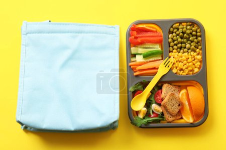 Téléchargez les photos : Sac et boîte à lunch avec de délicieux aliments sur fond jaune - en image libre de droit
