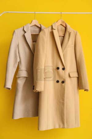 Photo for Stylish coats hanging on rack against yellow background, closeup - Royalty Free Image