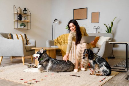Foto de Mujer joven con portátil y perros lindos en casa - Imagen libre de derechos