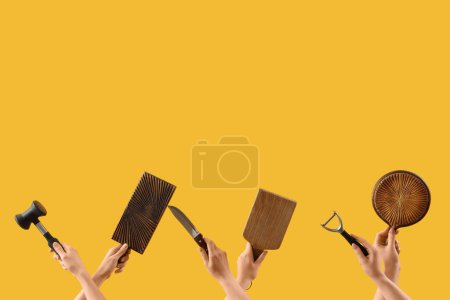 Photo for Female hands holding cutting board and different kitchen utensils on yellow background - Royalty Free Image