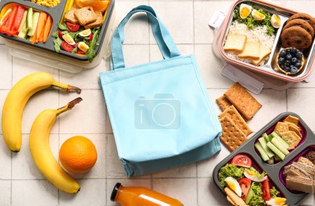 Téléchargez les photos : Sac et boîtes à lunch avec de délicieux aliments sur fond de tuiles blanches - en image libre de droit