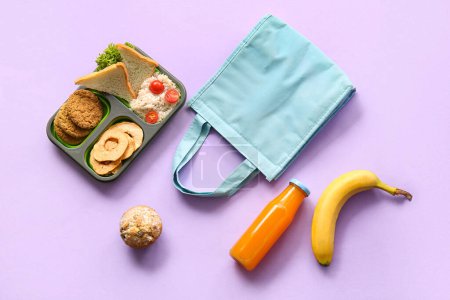 Téléchargez les photos : Sac, boîte à lunch avec de délicieux aliments et une bouteille de jus sur fond lilas - en image libre de droit