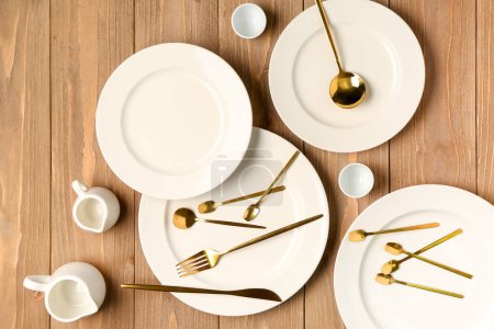 Photo for Clean plates, golden cutlery and pitchers on wooden table - Royalty Free Image