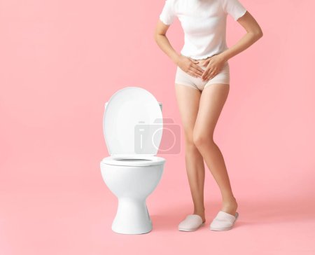 Téléchargez les photos : Jeune femme atteinte de cystite près de cuvette de toilette sur fond rose - en image libre de droit