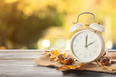 Photo for Alarm clock, acorns and autumn leaves on table outdoors. Daylight saving time end - Royalty Free Image