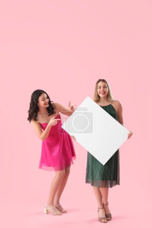 Foto de Mujeres jóvenes en vestidos con gran cartel en blanco sobre fondo rosa - Imagen libre de derechos