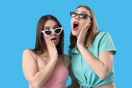 Foto de Amigos femeninos conmocionados en gafas de sol sobre fondo azul - Imagen libre de derechos