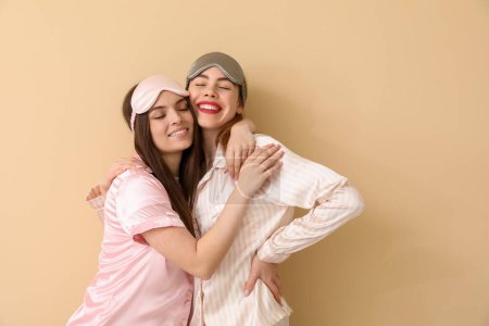Téléchargez les photos : Amis féminines avec des masques de sommeil étreignant sur fond beige - en image libre de droit