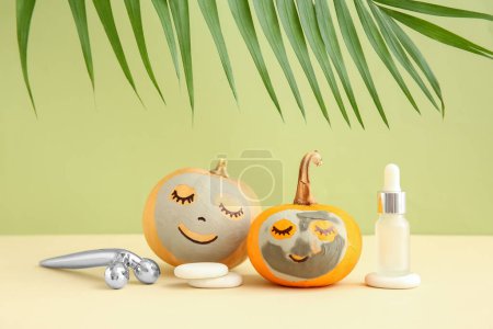 Foto de Calabazas con máscaras de arcilla, herramienta de masaje, piedras de spa y suero sobre la mesa sobre fondo verde - Imagen libre de derechos