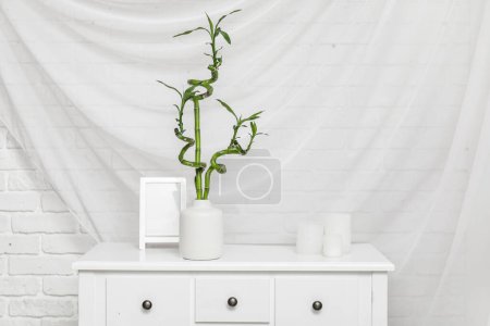Photo for Vase with bamboo stems, candles and blank picture frame on table against white fabric background - Royalty Free Image