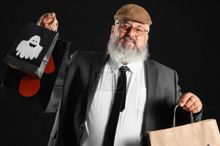 Téléchargez les photos : Homme mûr habillé pour Halloween avec des sacs-cadeaux sur fond noir - en image libre de droit