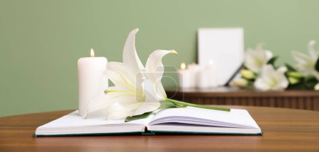Glowing candle, book and lily flower on table in room