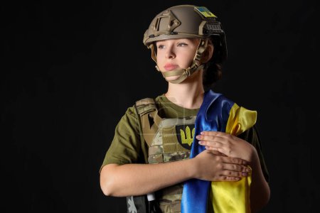 Junge Soldatin mit Fahne der Ukraine auf dunklem Hintergrund