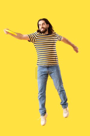 Photo for Jumping young man playing frisbee on yellow background - Royalty Free Image
