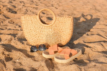 Foto de Chanclas con estilo con gafas de sol y bolsa de mimbre en la arena en el resort - Imagen libre de derechos