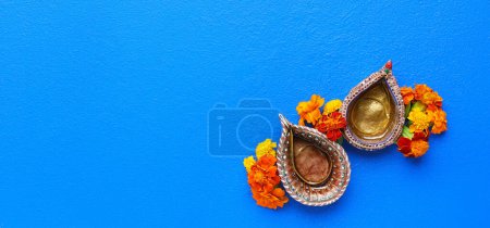 Photo for Diya lamps with marigold flowers on blue background with space for text. Divaly celebration - Royalty Free Image