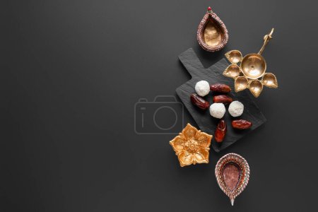 Photo for Diya lamps and board with treats on black background. Divaly celebration - Royalty Free Image