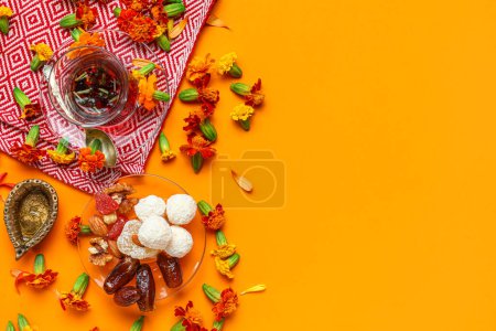 Photo for Diya lamp with marigold flowers, tea and plate of treats on orange background. Divaly celebration - Royalty Free Image