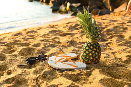 Foto de Chanclas con estilo con piña y gafas de sol en la arena cerca del océano en el resort - Imagen libre de derechos