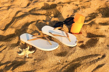 Foto de Chanclas con estilo con gafas de sol, crema de protección solar y estrellas de mar en la arena en el resort - Imagen libre de derechos