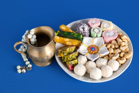 Photo for Diya lamp with jug, beads and plate of different treats on blue background. Divaly celebration - Royalty Free Image