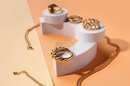 Decorative podiums with golden rings and necklace on color background