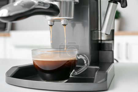 Modern coffee machine with glass cup of hot espresso on white table, closeup