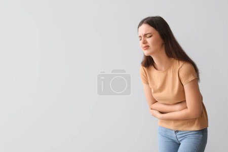 Foto de Mujer joven que sufre de dolor de estómago en el fondo claro - Imagen libre de derechos