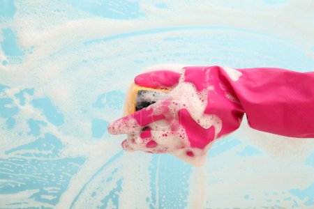 Photo for Female hand in pink rubber glove cleaning blue surface with sponge - Royalty Free Image