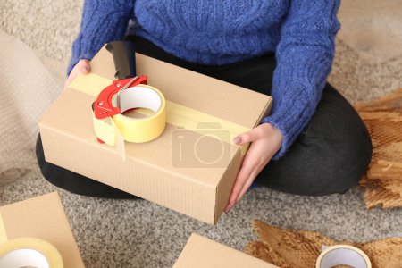 Foto de Mujer sentada en el suelo y sosteniendo la caja de cartón con dispensador de cinta de embalaje - Imagen libre de derechos