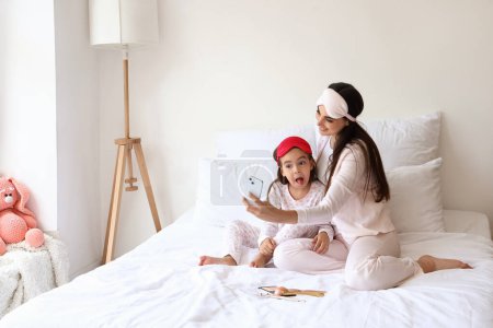 Téléchargez les photos : Mère heureuse et sa petite fille avec des masques de sommeil prenant selfie dans la chambre - en image libre de droit